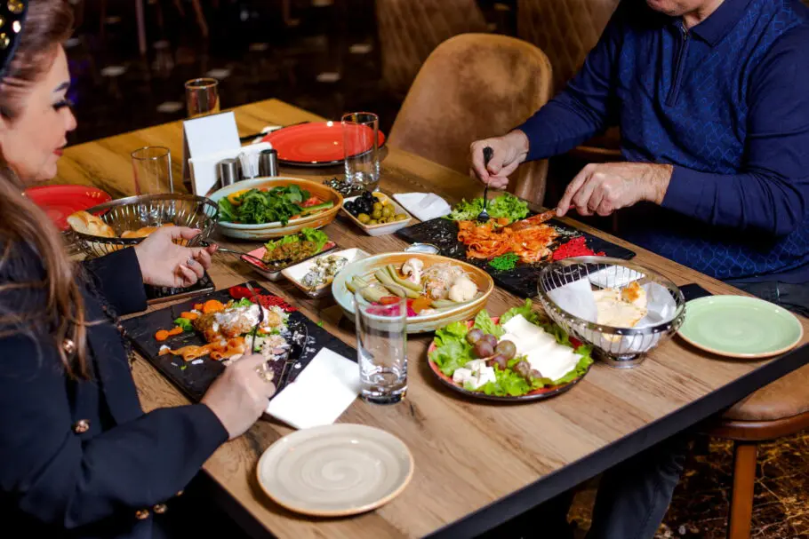 couple-have-dinner-with-pasta-salads-cheese-plate-pickles-olives